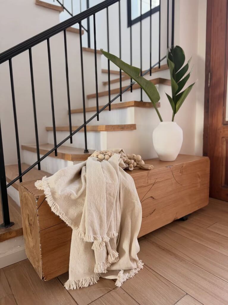 Detalle de un baúl de madera con manta de flecos y jarrón blanco al pie de la escalera de la casa de Noelia Marzol. Crédito : Instagram @noeliamarzolok
La casa de dos plantas está ubicada en un b