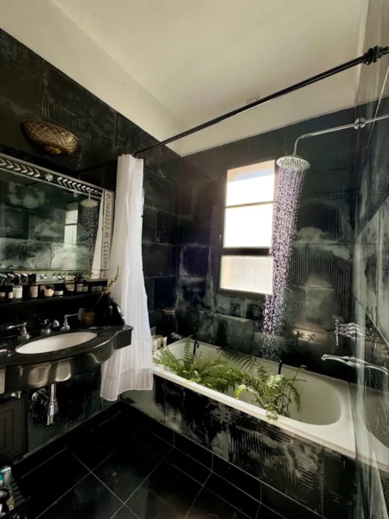  El baño, revestido íntegramente en cerámicos negros brillantes, contrasta con una bañera blanca y plantas junto a la ventana.
Fuente: Instagram @deboranishimoto