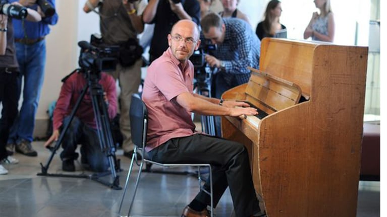 Fashion designer and founder of the Goodwood Vintage Festival, Wayne Hemmingway poses for photographers whilst playing a Challen upright piano from Abbey Road studios at Bonhams auction house in London on August 2, 2010. The piano once played by the Beatles and Pink Floyd has an estimated pre-sale value of 121 121 euro - 181 676 euro and will be auctioned during the Goodwood Vintage Festival on August 15, 2010. AFP PHOTO/ BEN STANSALL