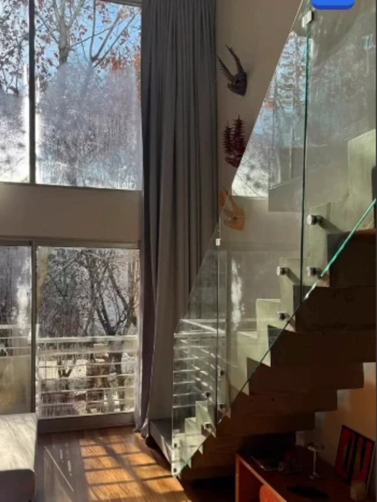 La escalera ya finalizada, con baranda de vidrio y estructura de madera, integrada a los ventanales del living. Fuente: Instagram.