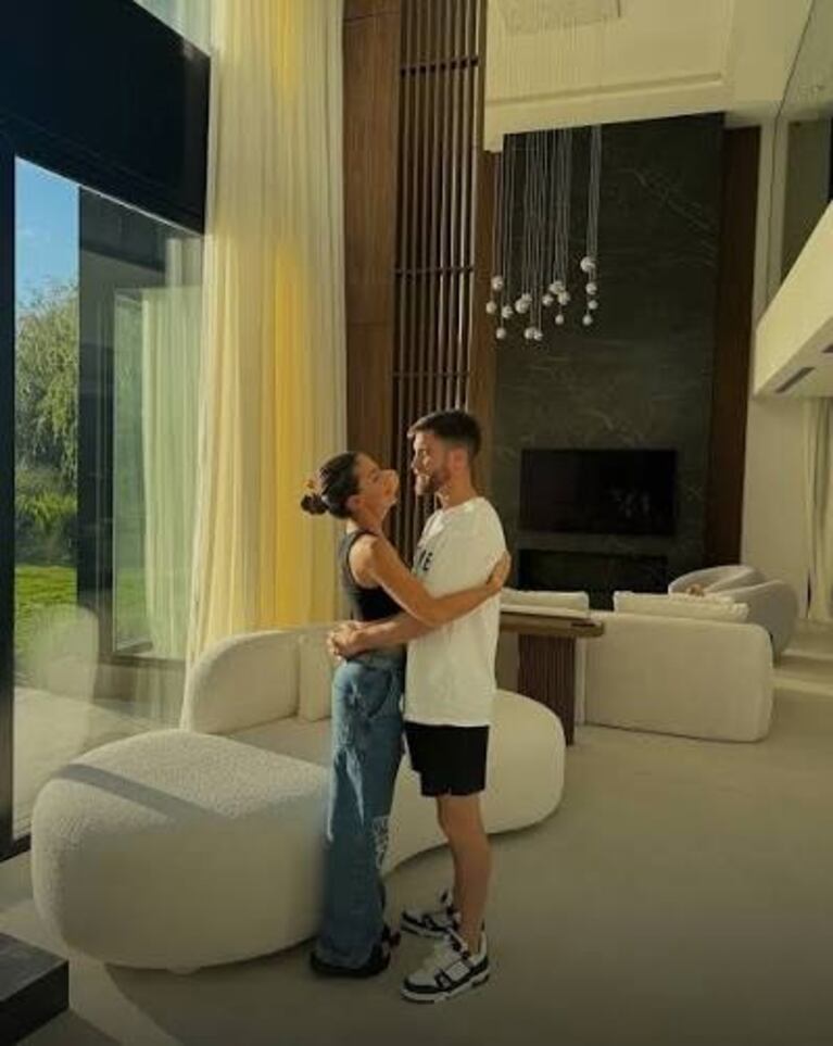 La pareja posó en el amplio living de la vivienda, con sillones color crudo, un ventanal al jardín y una chimenea de diseño moderno de fondo. Fuente: Instagram.
