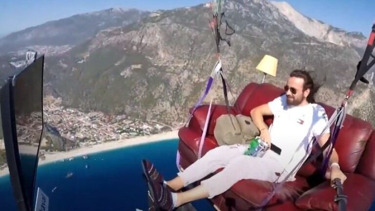 Un hombre vuela en parapente sentado cómodamente en un sofá mientras ve la tele