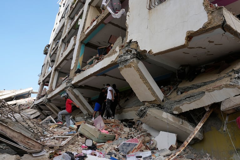 Varias personas caminan entre escombros dos días después de dos terremotos, el viernes 26 de junio de 2026, en Catia La Mar, Venezuela. (AP Foto/Fernando Vergara)